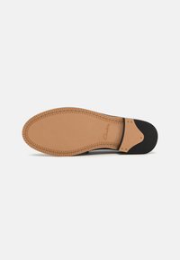Semelle de chaussure en cuir beige avec une finition lisse, dotée d'un talon en caoutchouc noir et d'un décor en couture le long du bord. Nom de la marque intégré.