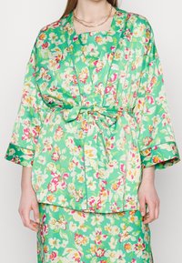 Zielona kwiatowa szata z szerokimi rękawami i materiałowym paskiem. Posiada wielokolorowe wzory kwiatowe oraz gładką, błyszczącą teksturę.