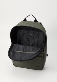 Mochila verde olivo con un interior negro; cuenta con un compartimento principal con cremallera, un asa en la parte superior y un bolsillo interior para organización.