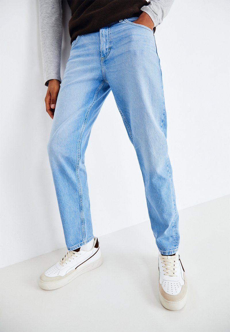 Jeans in denim azzurro chiaro con taglio dritto e texture sbiadita. Indossati con sneaker bianche con accenti in beige e marrone.