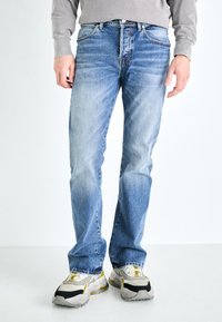 Vaqueros de mezclilla azul claro con corte recto, acabado desgastado y costuras en contraste, combinados con zapatillas gruesas en gris y amarillo.
