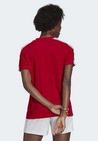 Rotes Sport-T-Shirt mit kurzen Ärmeln, das weiße Akzente an den Schultern und einen runden Ausschnitt aufweist, aus einem glatten, leichten Stoff gefertigt.