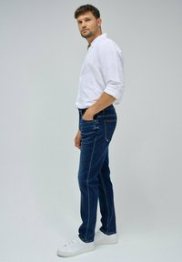 Jeans de mezclilla azul ajustados con un corte recto clásico, combinados con una camisa blanca de botones y zapatillas blancas. Diseño simple sin patrones visibles.