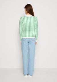 Maglione a fantasia a rombi verde e bianco con collo rotondo, vestibilità slim e polsini a coste, abbinato a jeans a gamba larga di colore azzurro chiaro.