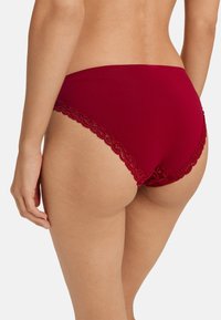 Brief rossi in cotone con rifiniture in pizzo, caratterizzati da un design a vita alta e una consistenza liscia, con un bordo in pizzo floreale intricato lungo le aperture delle gambe.