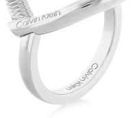Sølvfarget ring med en vridd design og en glatt ring, merket med "Calvin Klein" på innsiden, som fremhever den polerte overflaten.
