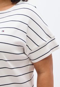 Λευκό βαμβακερό μπλουζάκι με ναυτικό οριζόντιο ρίγες, στρογγυλή λαιμόκοψη και κοντά μανίκια. Διαθέτει ένα μικρό λογότυπο στο στήθος.