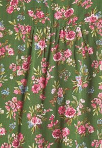 Tissu floral vert, présentant des fleurs roses, bleues et blanches. Texture douce avec des plis visibles, créant un design doux et fluide.