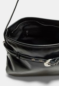Schwarze Leder-Umhängetasche mit Schnallendetail, offenes Oberteil, das eine innere Reißverschlusstasche und eine glatte, strukturierte Innenauskleidung zeigt.