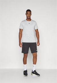 Lys grå t-skjorte med korte ermer og en svart logo, kombinert med svarte shorts med branding-aksent, hvite sokker og svarte treningssko.
