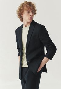 Marinblå kavaj med två knappar, strukturerade slag, enkel bröstficka och slim fit. Matchad med en ljusgrön t-shirt.