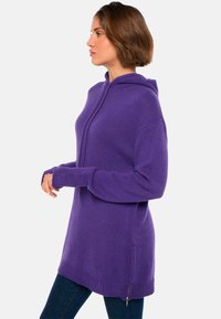 Lila Kapuzenpullover mit lockerer Passform, gerippten Bündchen und einem Reißverschlussdetail an der Seite, aus weichem, strukturiertem Stoff.