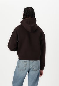 Sweatshirt à capuche brown avec un design court. Il présente des manches longues, un ourlet côtelé et est associé à un jean en denim bleu clair.