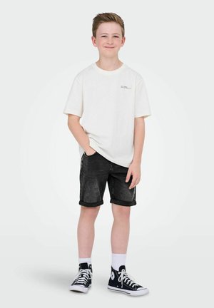 Ljus beige bomulls-t-shirt med korta ärmar, som är ihopparad med mörka denimshorts och svarta hög-toppsneakers med vita detaljer och strumpor.