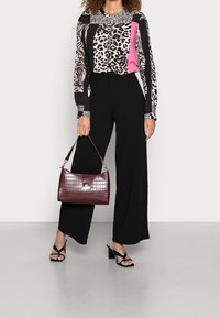 Svarta vida byxor i kombination med en mönstrad blus som har djurtryck och rosa detaljer. Håller en burgundy handväska i faux-krokodil.