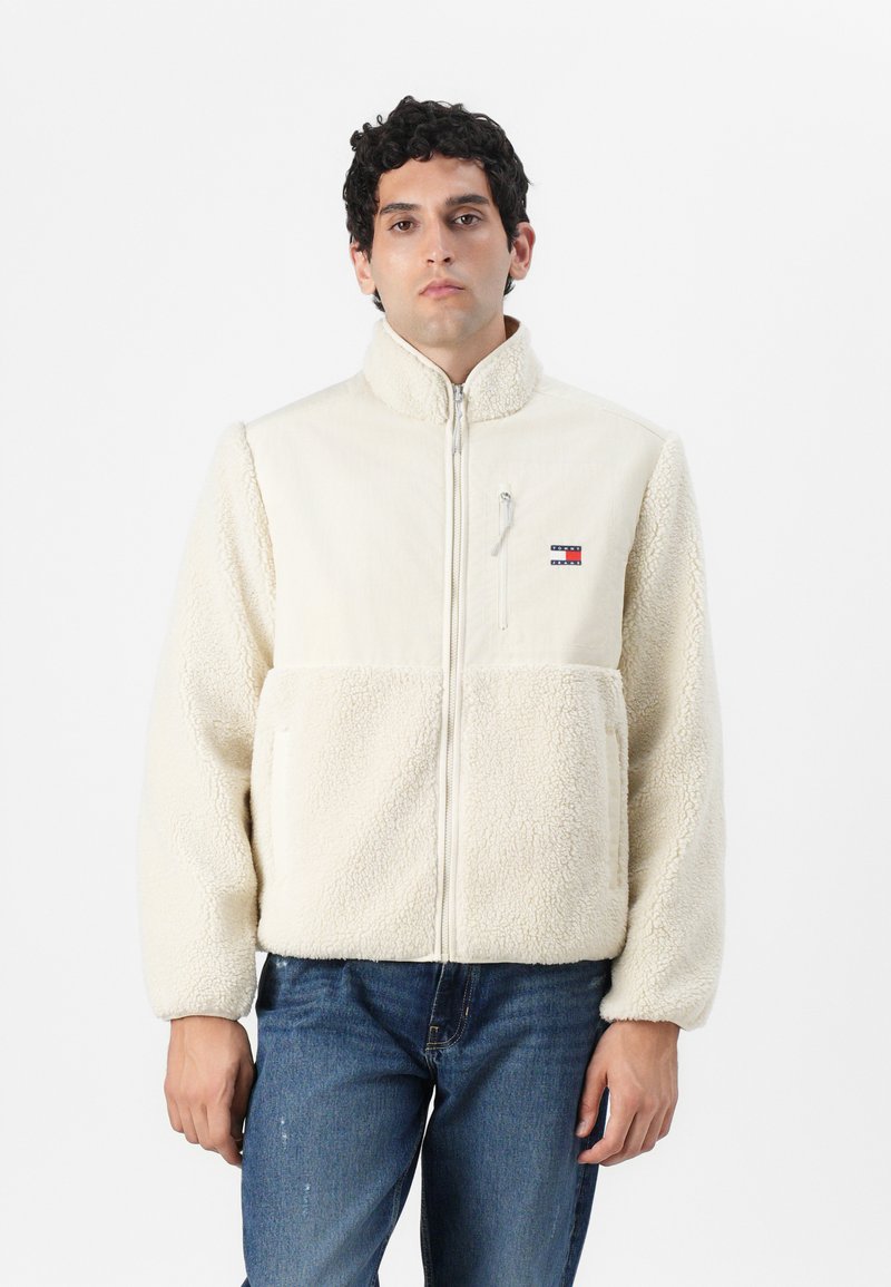 Fleecejakke i off-white med glidelås, høy krage og en brystlomme. Har en myk tekstur og kontrastpanel i stoff.