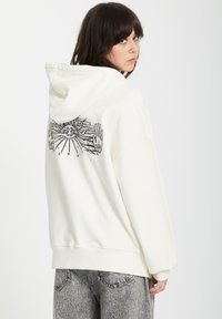 Felpa bianca con stampa grafica raffigurante mani e un sole sul retro. Tessuto morbido, vestibilità comoda e cappuccio con cordino.