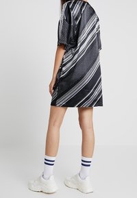 Svart satin klänning med diagonala vita ränder, prickar och en lös passform. Parat med vita sneakers och randiga strumpor.