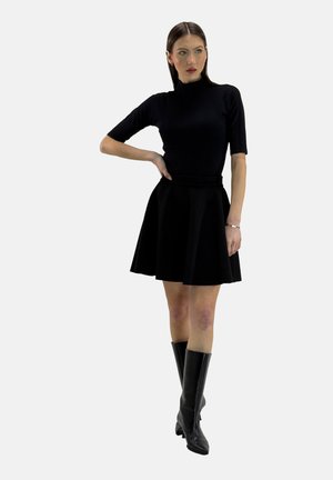 Zwarte aansluitende turtleneck top, gecombineerd met een zwarte uitlopende rok, aangevuld met kniehoge leren zwarte laarzen, wat een slanke silhoutte creëert.