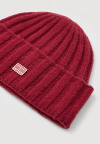 Punane sooniline müts, millel on volditudäär ja väike ristkülikukujuline Tommy Jeans logo silt ääres.