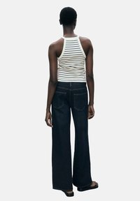 Striped, ribbed tank top and high-waisted, wide-leg dark denim jeans; tank features thin straps, jeans have structured pockets.