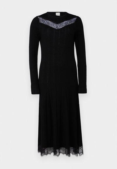 Vestido de malha preto com mangas longas, corpete justo, saia rodada e acabamento em renda. Apresenta um padrão decorativo costurado ao longo da linha do pescoço.