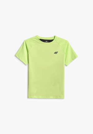 Garçon debout souriant, portant une chemise vert citron à manches courtes, un pantalon noir et des baskets noires sur un fond gris.
