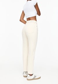 Jean taille haute beige clair avec une coupe droite et deux poches arrière, associés à des baskets blanches et un top blanc court.