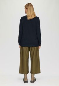 Marineblauwe gebreide trui met lange mouwen, gecombineerd met olijfgroene wijde broek. De outfit wordt afgemaakt met doorzichtige enkellaarsjes en een minimalistisch ontwerp.