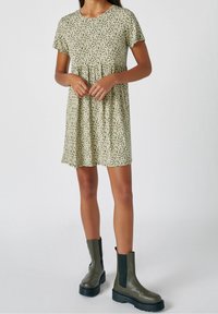 Robe à imprimé floral en vert et blanc, manches courtes, taille froncée. Associée à des bottines kaki avec semelles épaisses noires.