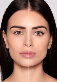 Połowa twarzy pokazuje naturalny kolor skóry bez makijażu; druga połowa ma tusz na rzęsach, podkreślający ich wyrazistość. Gładkie włosy, neutralne tło.