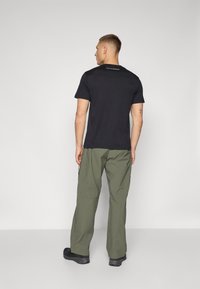Black short-sleeve t-shirt with a crew neck, paired with loose-fitting olive green pants and black footwear, viewed from the back.