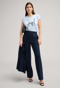 Blauw-wit gestreepte korte mouw T-shirt met "Joop!" print, gecombineerd met marineblauwe wijde broek en zwarte haksandalen.