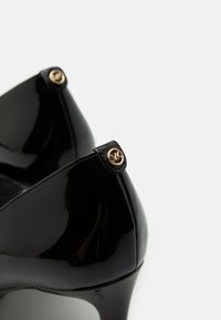Escarpins en cuir verni noir avec un bout pointu, une finition brillante et des accents en or sur le talon. Design élégant à talon aiguille.