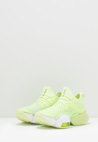 Limevihreät urheilukengät hengittävällä verkko-yläosalla, tekstuurilla koristeltu, valkoisilla yksityiskohdilla ja näkyvällä ilmatyynyllä pohjassa.