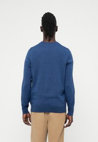 Kék kötött pulóver hosszú ujjakkal, kerek nyakkivágással és sima textúrával. Minimális díszítés, letisztult vonalak és laza szabás.