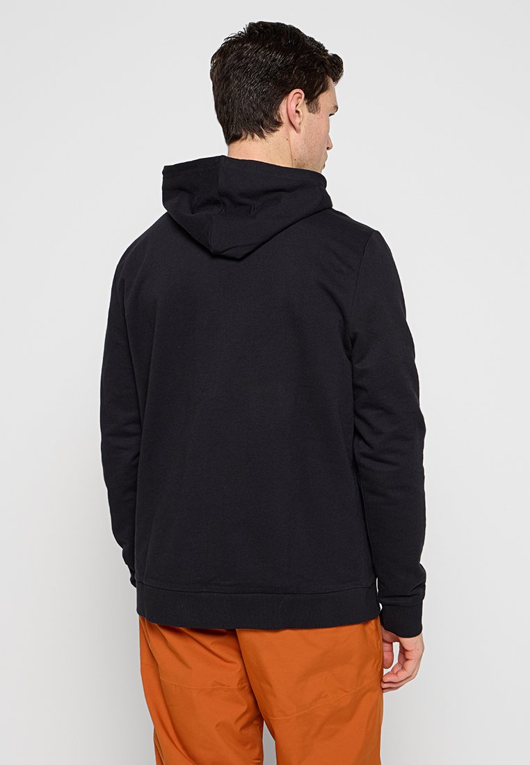 Felpa nera con cappuccio realizzata in morbido tessuto, caratterizzata da un design semplice e polsini a costine, abbinata a pantaloni arancioni per creare un contrasto.