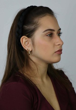 Fascia intrecciata nera, orecchini a cerchio dorati, rossetto marrone e trucco naturale su sfondo semplice. Capelli lisci e lunghi.