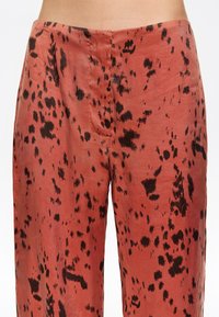 Pantalones holgados en color óxido con manchas abstractas negras. Compuestos de una tela ligera con una textura suave y un ligero brillo.
