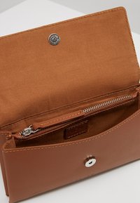 Ruskea nahkalompakko, jossa on napitus, sileä pinta, sisäpuolella vetoketjullinen tasku ja vaaleamman sävyinen kangasvuori.