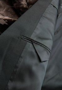Schwarzer, strukturierter Stoff mit glatter Oberfläche, der auf der linken Seite eine dekorative Falte und auf der rechten Seite einen kontrastierenden, gestreiften Bereich aufweist.