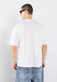 Vit bomullströja med korta ärmar, avslappnad passform och rundad halsringning, kombinerad med ljusblå denimjeans, minimal detaljering.