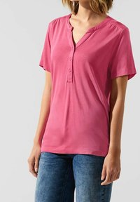 Maglietta henley rosa a maniche corte con chiusura a bottoni e delicati gather sulle spalle, realizzata in un tessuto leggero e liscio.