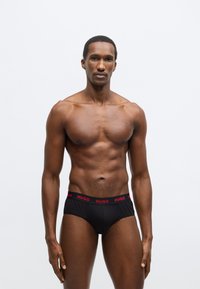 Čierne boxerky s červeným pásom s nápisom "HUGO". Hladká látka, priliehavý strih a štandardný výstrih. Jednoduchý a minimalistický štýl.