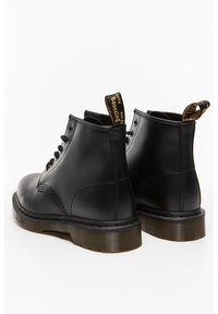 Botas de tobillo de cuero negro con puntera redondeada, cordones en la parte delantera y una lengüeta amarilla en la parte posterior. Cuentan con una suela de goma gruesa con un acabado texturizado.