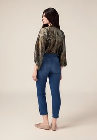 Blusa fluida y con estampado en tonos tierra, jeans oscuros de cintura alta con aberturas en los tobillos, y bailarinas beige. Tejido suave y ajuste holgado.
