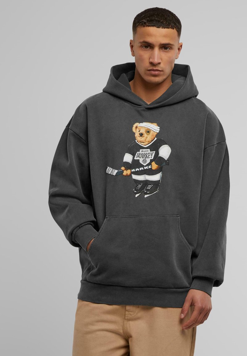 Tumši pelēks hoodie, kas izgatavots no mīkstas kokvilnas, ar lāča grafiku sporta ekipējumā, priekšējo kabatu un ribotām aprocēm un apakšmalu.