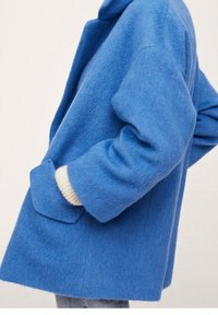 Abrigo de mezcla de lana azul con una silueta relajada, que presenta un cuello alto, grandes bolsillos laterales y acentos de punto crema en los puños.