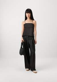 Top in satin nero con spalline sottili, sovrapposto a una vestibilità più ampia. Abbinato a pantaloni neri larghi e una borsa nera texture. Scarpe beige.