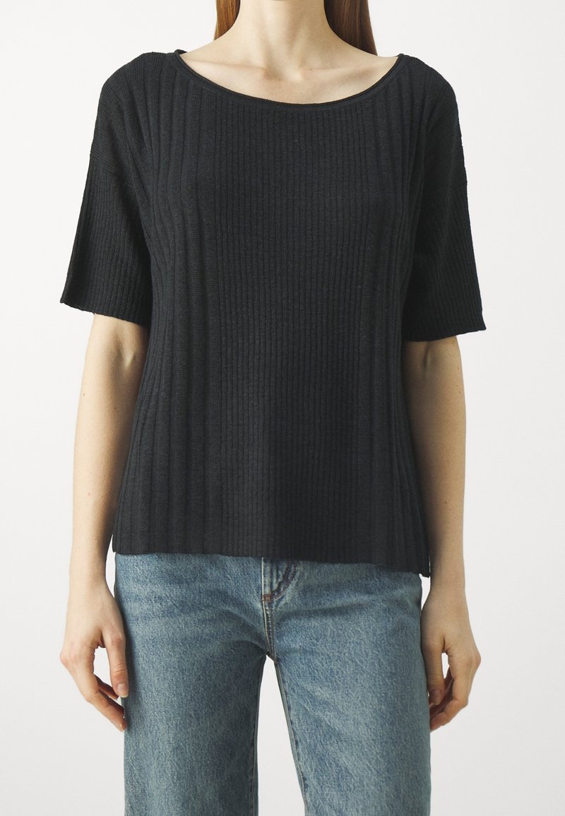 Haut court à manches courtes en maille côtelée noire avec un large col en U, présentant une coupe décontractée et un tissu texturé. Porté avec un jean denim bleu clair.